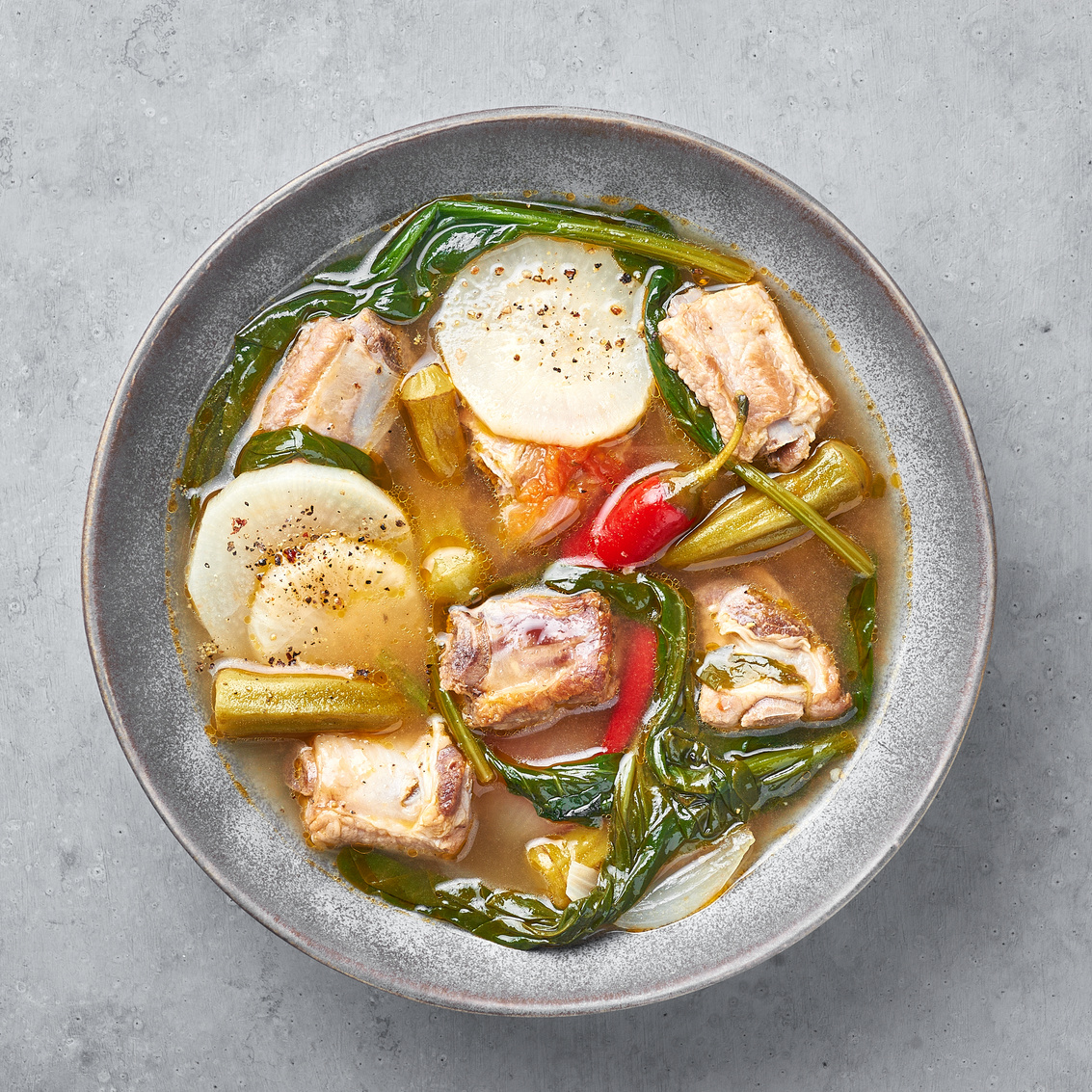 Sinigang na Baboy dish or Filipino Pork Meat Soup in gray bowl on concrete backdrop. Filipino Food. Asian Meal